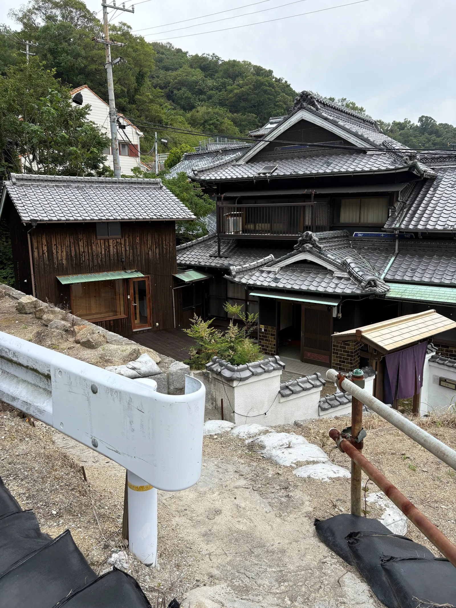 Tiled roofs of traditional houses packed along a wooded hillside in a Japanese village.