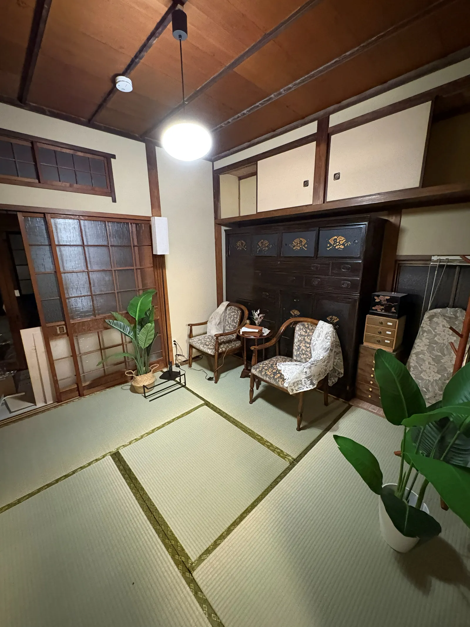 A restored tatami room with exposed timber ceiling beams, paper screens and an antique wooden chest.